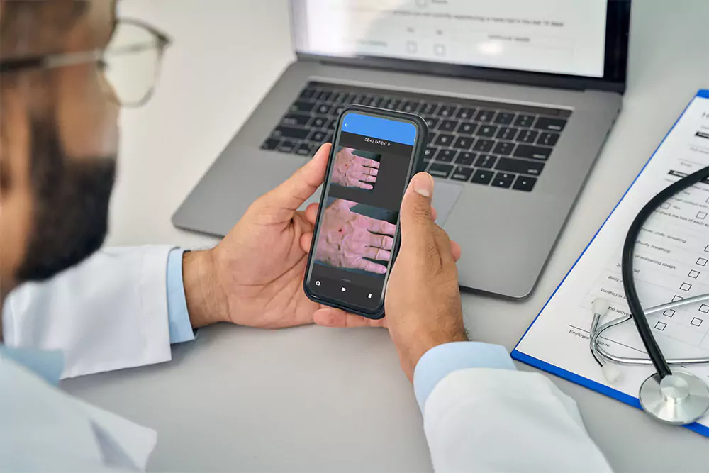 A healthcare professional using a smartphone to capture clinical images with a laptop