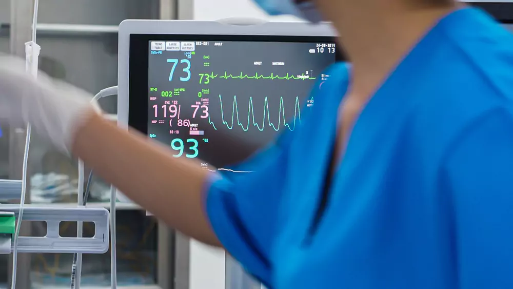 A healthcare professional is monitoring a patient's vital signs on a bedside monitor.